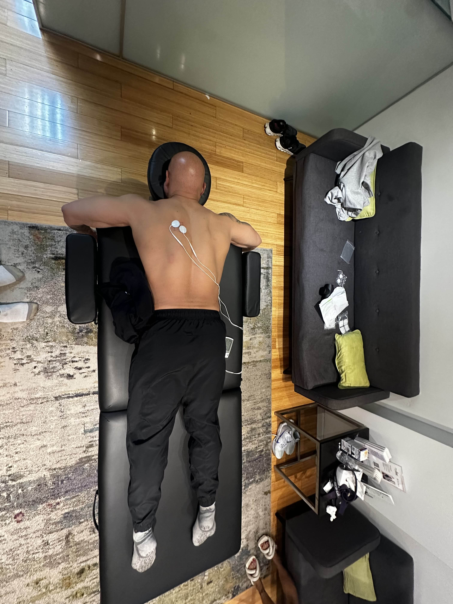 Client face down on black table with stim pads and massage gun nearby